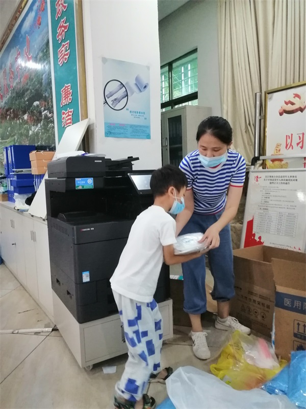 图为梁启秀与儿子一起搬运防疫物资